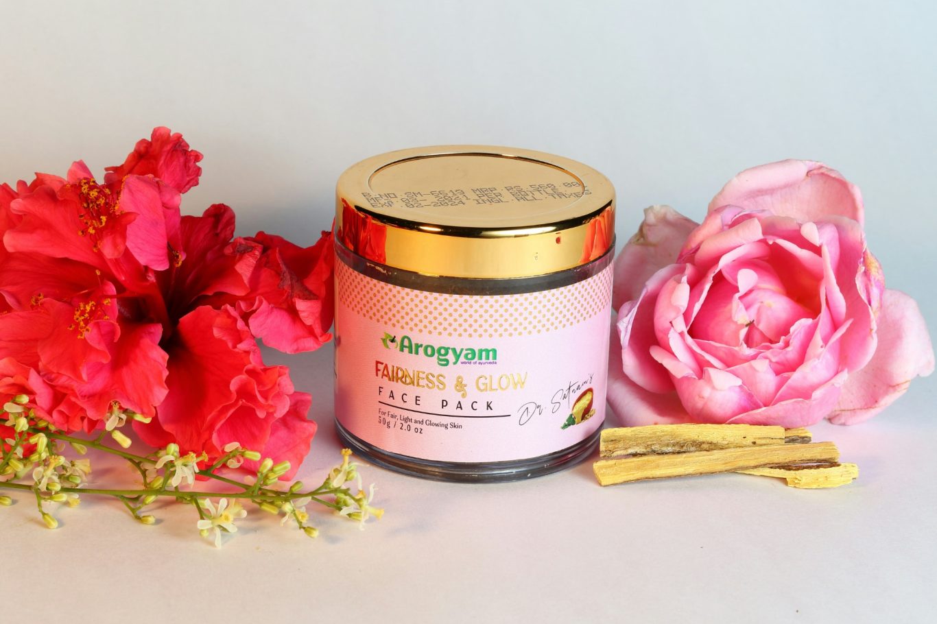 Barattolo di crema per la pelle con fiori rosa e rametti verdi accanto. 