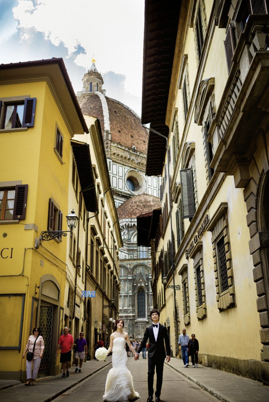 Sposa e sposo camminano in una strada di Firenze con la cattedrale sullo sfondo.