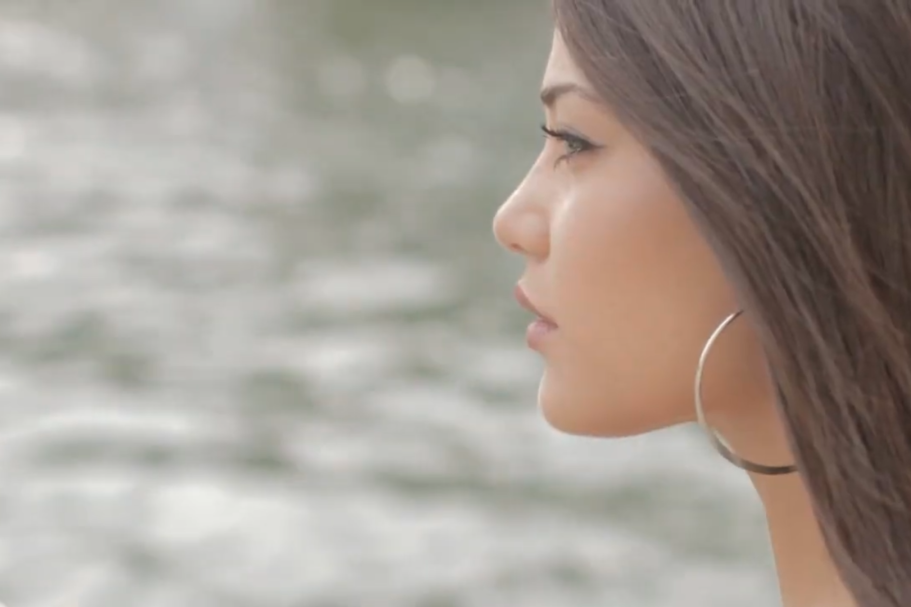 Profilo di una giovane donna con i capelli lunghi, che guarda pensierosa vicino all'acqua.