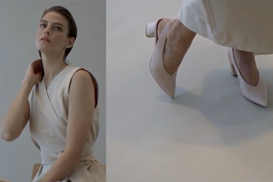 Model in a light dress adjusts her hair, showcasing elegant high-heeled shoes.