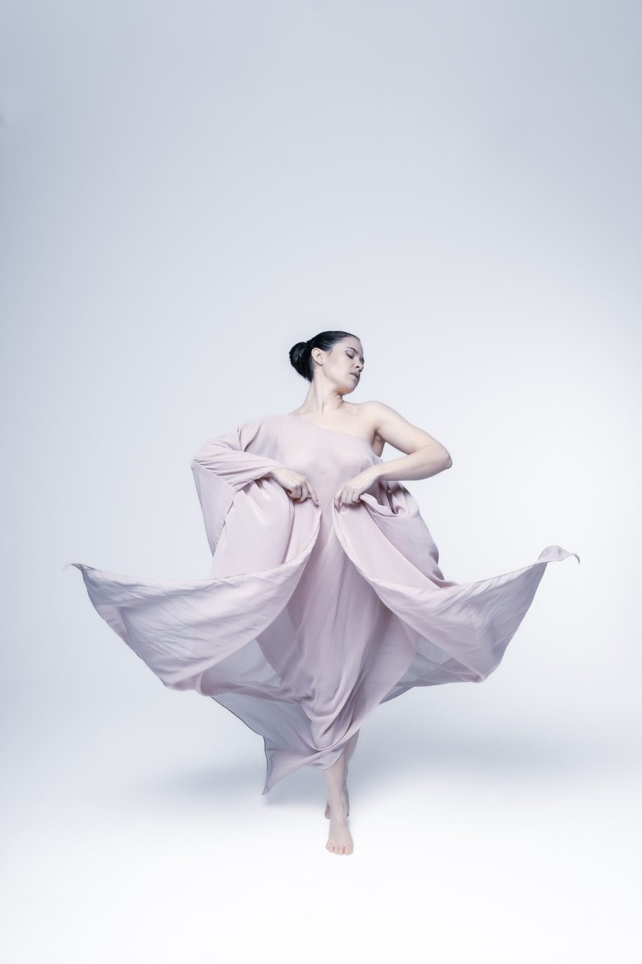 Ballerina in abito rosa fluido, in movimento aggraziato su sfondo chiaro.