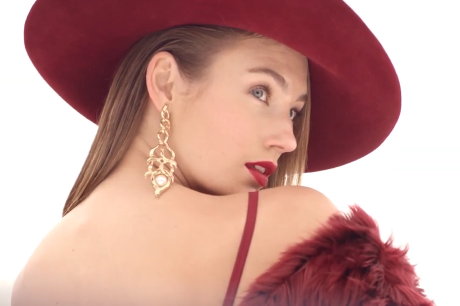 Donna con cappello rosso, orecchini, trucco elegante e sguardo di profilo.