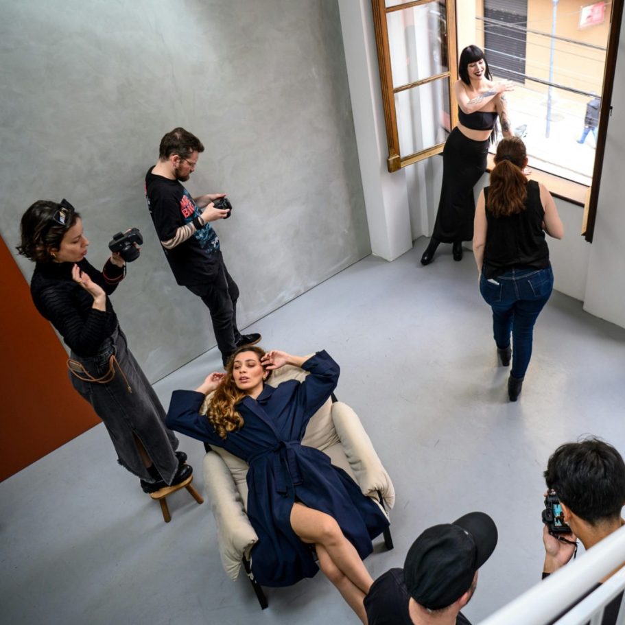 Servizio fotografico di moda con una modella in posa su una sedia e fotografi che catturano la scena.