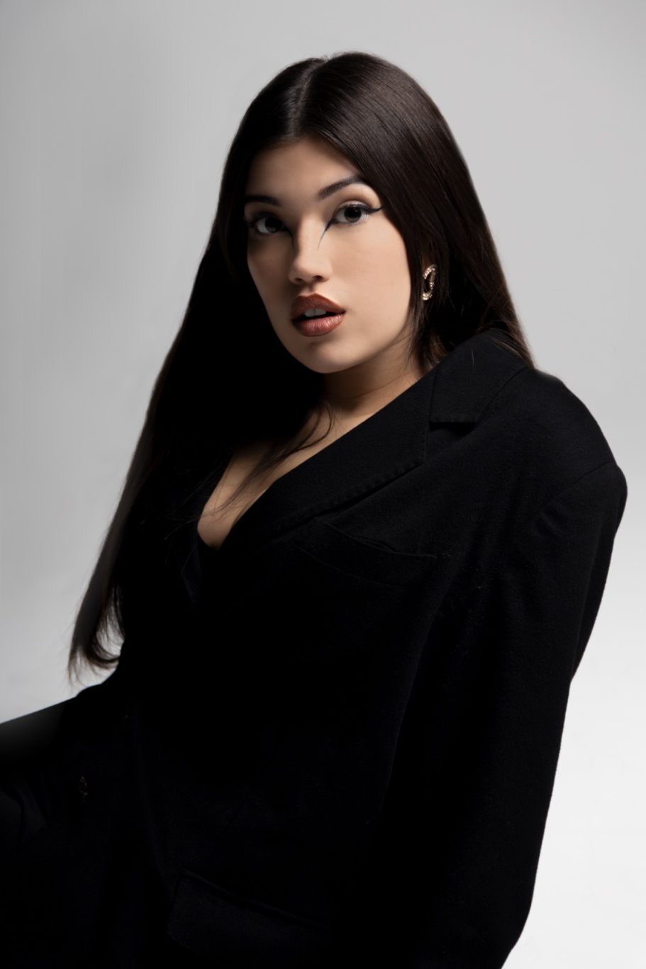 Giovane donna con lunghi capelli scuri, che indossa un vestito nero, guardando direttamente la telecamera.