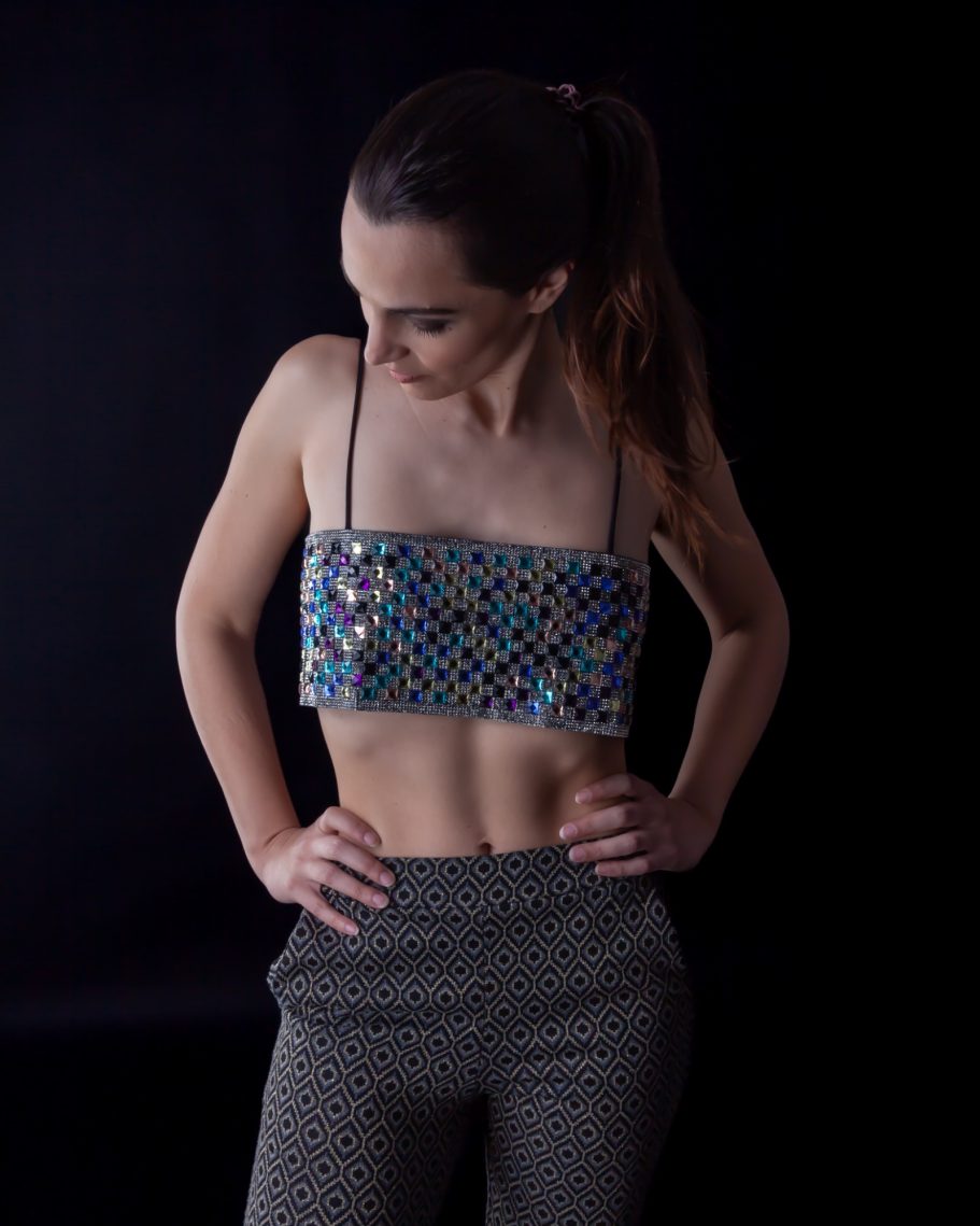 Modella che indossa un elegante top corto fantasia e pantaloni aderenti su uno sfondo scuro.