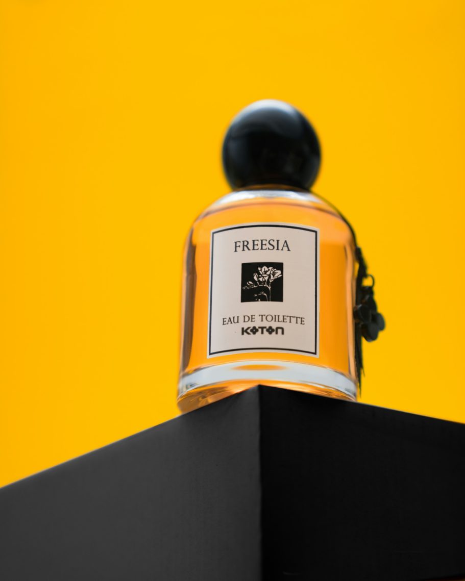 Bottiglia di profumo con un tappo nero su un piedistallo nero su uno sfondo giallo. foto prodotto professionale ad Alessandria 