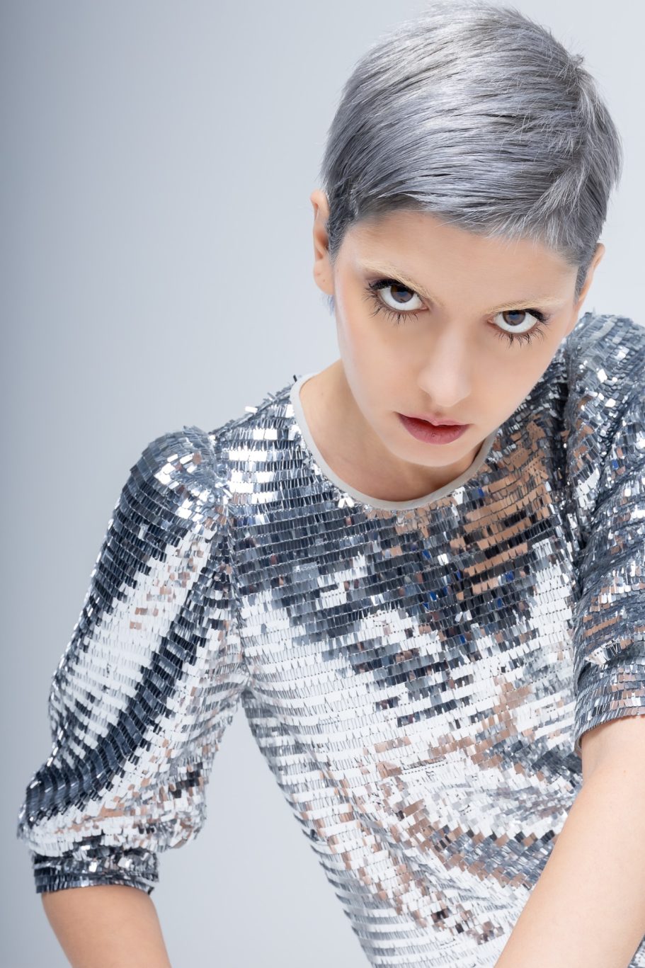 Modella con capelli corti e grigi, indossa una maglia di paillettes argentate, sguardo intenso.