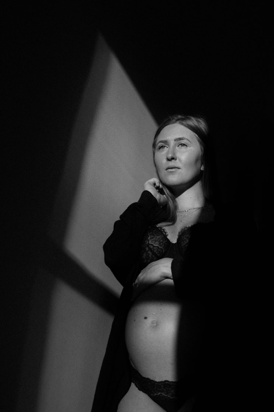 Donna incinta in lingerie nera, illuminata da ombre morbide. foto di maternity ad Alessandria