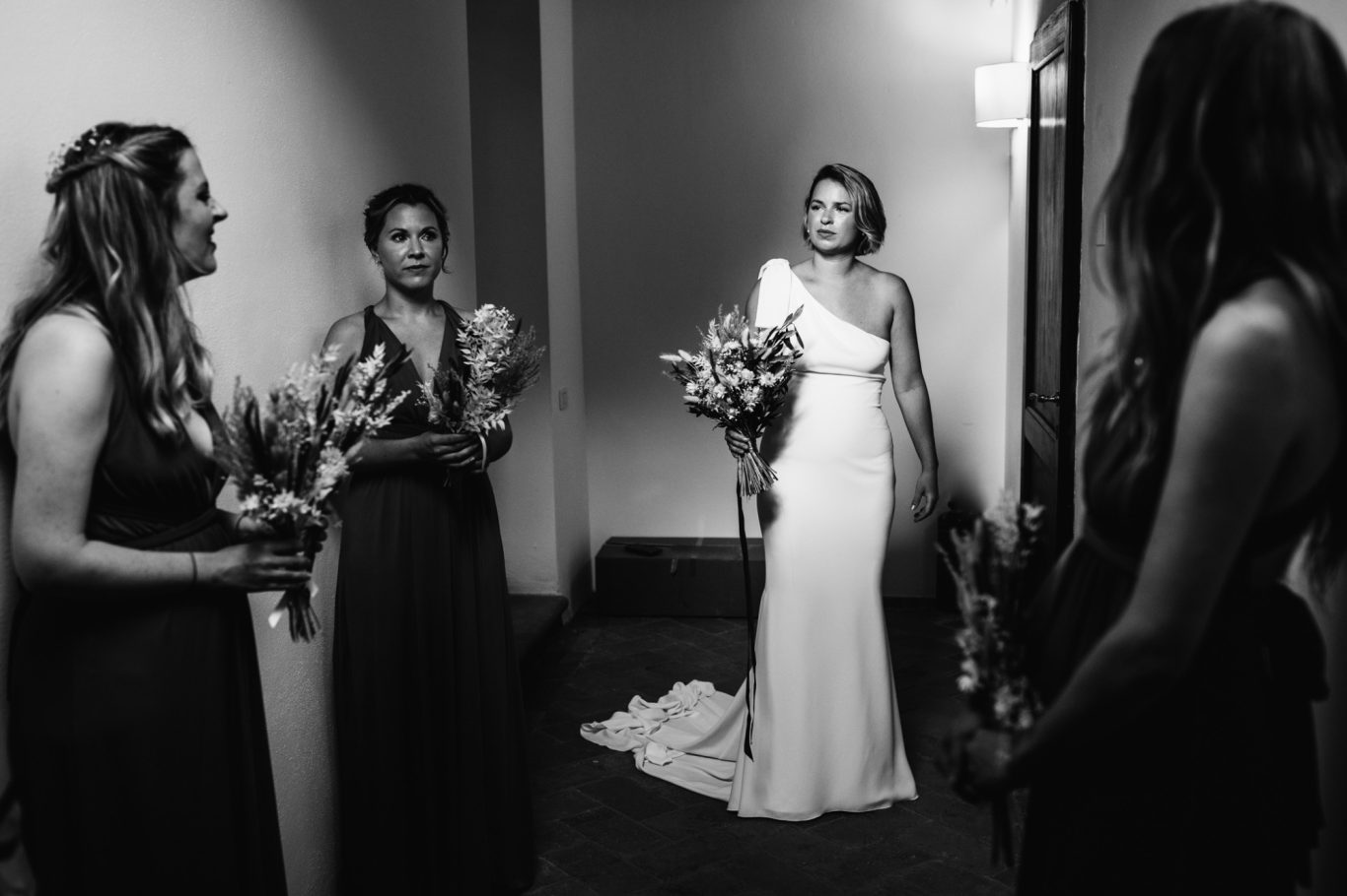 Sposa in abito bianco con bouquet, circondata da quattro damigelle in abiti eleganti.